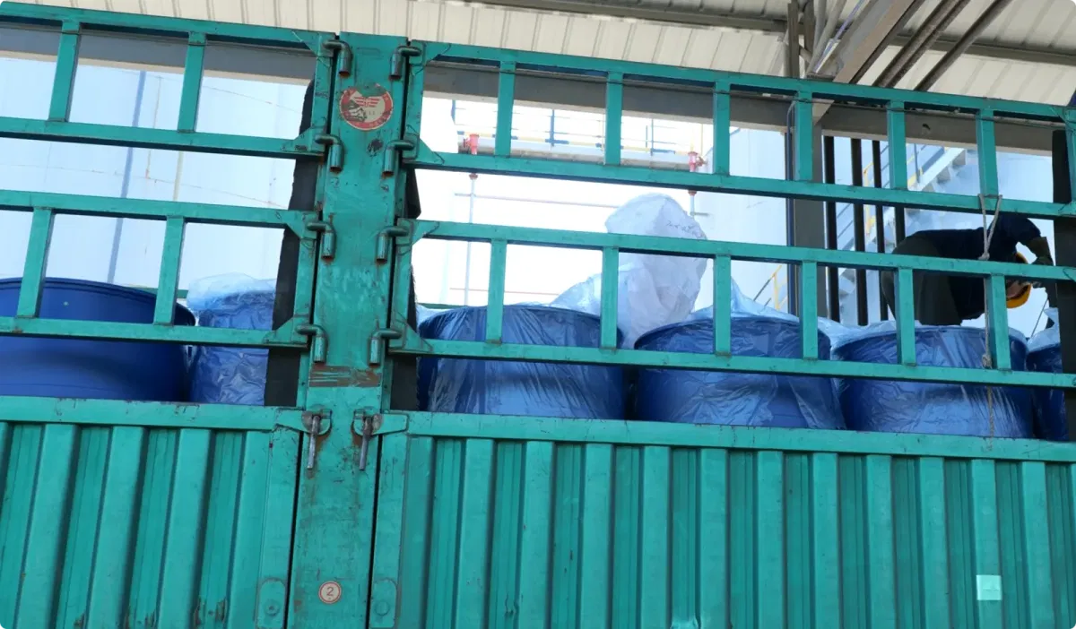 Worker inspecting sealed 200L blue plastic drums of DOTP before export shipment